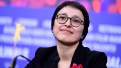 شهربانو سادات درحالی که لبخند کوتاه به لب دارد و پیراهن سیاه و عکس پوشیده در جشنواره فیلم برلین حضور دارد. 