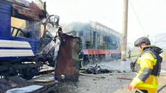 Сотрудник экстренных служб смотрит на обгоревший поезд