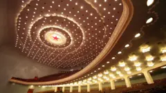 Imagem do interior de um auditório mostra um teto repleto de luzes brancas e uma estrela vermelha com um círculo iluminado no centro. Também é possível ver fileiras de assentos.