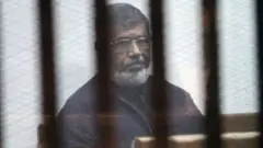 CAIRO, EGYPT - FEBRUARY 26: Egypts ousted President Mohamed Morsi attends a trial session over the Wadi el-Natrun prison case at Cairo Police Academy in Egypt on February 26, 2017. (Photo by Moustafa El Shemy/Anadolu Agency/Getty Images)