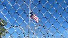 Uma bandeira americana tremulando no céu azul atrásjoguinho que paga no pixuma cercajoguinho que paga no pixarame farpado na Baíajoguinho que paga no pixGuantánamo