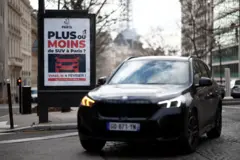 Um SUV passa por um cartaz em Paris divulgando uma votação em 2024 sobre o aumento das taxas de estacionamento para reduzir as emissões e aumentar a segurança dos pedestres