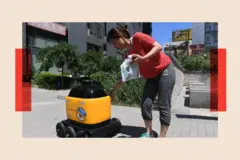 Una mujer recoge la compra entregada por un robot de reparto de Zhen Robotics en un complejo residencial.