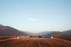 Bodega de arquitectura moderna integrada en un valle con viñedos y montañas al amanecer.