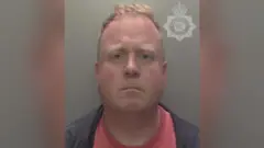Undertaker Robert Bush stares at the camera in a police mugshot. He has a neutral expression, his mouth slightly down-turned and a faint frown.