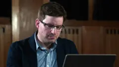 Homem de óculos olha para o laptop aberto