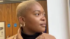 Mulher negra com cabelo quase raspado olha para a direita