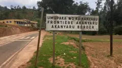 Icyapa kigaragaza umupaka wo ku Kanyaru hagati y'u Rwanda n'u Burundi, ku ruhande rw'u Rwanda, inyuma hagaragara abantu bacye
