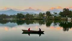 पोखरास्थित फेवातालमा डुङ्गा र पृष्ठभूमिमा हिमाल 