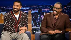 O ator Michael B. Jordan e o cineasta Ryan Coogler durante uma entrevista em 2/4/2025. Jordan veste um cardigã marrom estampado, enquanto Coogler usa uma jaqueta marrom xadrez