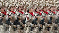 Mujeres soldados con uniforme militar y sombreros marchan con rifles