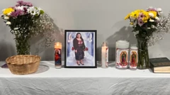 Uma mesa com uma foto da falecida, María Florinda Ríos Pérez, ao lado de velas e vasos de flores.