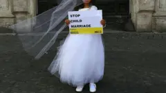 Atriz infantil vestida de noiva, com um cartaz dizendo 'Parem com o casamento infantil', em inglês