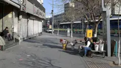 خیابان انقلاب تهران مغازه ها بسته است. یک گلفروش کنار خیابان نشسته ولی مشتری ندارد. یک نفر هم روی پله های یک شرکت نشسته. خیابان تقریبا خالی است. 

ساکنان میدان انقلاب، یکی از شناخته‌شده‌ترین نقاط تهران، ایران، در تاریخ سه شنبه ۲۶ اسفند ۱۴۰۴ به زندگی روزمره خود ادامه می‌دهند، پس از آن‌که ایالات متحده و اسرائیل درشنبه ۹ اسفند ۱۴۰۴ حملات گسترده‌ای علیه اهداف مختلف در ایران انجام دادند که به کشته شدن آیت‌الله علی خامنه‌ای، رهبر عالی ایران و آسیب به ساختمان‌ها و خودروهای بسیاری انجامید.