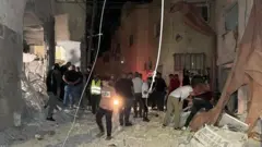 Abantu bagenda iruhande rw'inyubako yangijwe n'igitero cya Israel i Jenin 