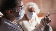 A doctor prepares a vaccine to give to a senior woman at her home