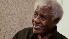 Tony Tornado é um homem negro de cabelos brancos. Na foto ele está sorrindo e olhando para o lado