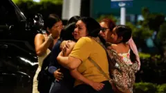 Un grupo de mujeres llorando y abrazándose a las afueras del Aeropuerto Internacional José Joaquín de Olmedo, después de que un hombre fuera abatido a tiros y otro resultara herido el 17 de junio de 2026.