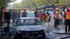 පකිස්ථාන අගනුවර පිහිටි අධිකරණ පරිශ්‍රයක් ඉදිරිපිට සිදුවූ බෝම්බ ප්‍රහාරයෙන් පසුව ගිනි ගන්නා ලද මෝටර් රථයක් නිවීමට ගිනි නිවන භටයින් උත්සහ දරන ආකාරය 