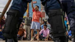 गत भदौ २४ गतेको जेन जी आन्दोलनमा सहभागीहरू। प्रहरीको कम्मरभन्दा मुनिको भागको पृष्ठभूमिमा केही व्यक्तिहरू धर्नामा बसिरहेको देख्न सकिन्छ।