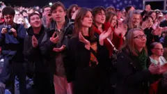 Foto mostra jovens e mulheres aplaudindo.