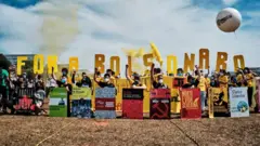 Manifestantes seguram letras amarelas onde se lê 'Fora Bolsonaro', além de cartazes com capas de livros