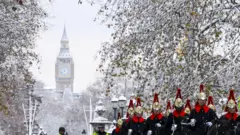 Członkowie gwardii królewskiej jadą pod ośnieżonymi drzewami przed Wieżą Elżbiety, powszechnie znaną jako Big Ben, podczas gdy mroźna pogoda utrzymuje się w Londynie