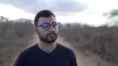 Homem jovem de óculos, com paisagem semiárida ao fundo