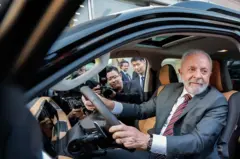 Lula usando terno sentado dentro de um veículo chinês