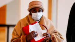 Agatha Kanziga Habyarimana, umupfakazi w'uwari Perezida w'u Rwanda Juvénal Habyarimana, ubwo yari ageze ku rukiko i Paris mu Bufaransa, ku itariki ya 3 Ugushyingo (11) mu mwaka wa 2020, kugira ngo yumvwe ku ruhare uwari umujandarume w'Umufaransa Paul Barril ashinjwa kugira muri jenoside yabaye mu Rwanda mu 1994. Agathe Kanziga yambaye agapfukamunwa, ingofero y'ikigina na fulari y'ikigina yiteye mu bitugu, ndetse afite inyandiko afatiye imbere. 
