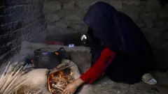 تصویر زنی در حال آتش کردن در زیر دیگدان. صورت این زن نمایان نیست و تنها در تصویر دیده می شود که به زیر دیگدانی آتش روشن می کند. 