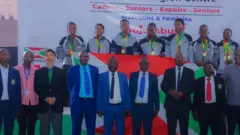 Abakinnyi b'ikipe y'igihugu ya karate y'u Burundi bahagaze inyuma hejuru y'abandi bagabo biganjemo abambaye amakositimu na karuvati. Abakinnyi b'u Burundi bambaye imidali mu ijosi ndetse bambaye amajaketi ariho ibendera rito ry'u Burundi