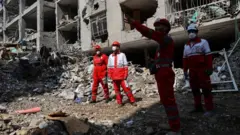 इराणची राजधानी असलेल्या तेहरानमध्ये हवाई हल्ल्यात उदध्वस्त झालेल्या एका इमारतीत रेड क्रॉसच्या बचाव दलाचे सदस्य
