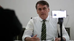 Bolsonaro, sentado diante de mesa, fala para câmera de celular