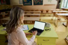 Professora usando laptop em sala de aula vazia