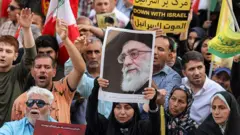 Manifestante exibe uma imagem do líder supremo do Irã, o aiatolá Ali Khamenei, reunido com outras pessoas durante uma manifestação em solidariedade ao governo iraniano contra os ataques de Israel ao país