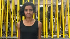 Melani Gunathilaka in front of railings with police behind her