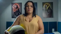 Thais é uma mulher branca,betsbola o bom do futebol apostacabelos escuros e lisos na altura dos ombros. Está vestindo um macacão claro e usa um colar com um pingente escrito "fé". Na foto, ela segura um capacete amarelo. No fundo, uma cama com uma colcha azul e três quadros com fotosbetsbola o bom do futebol apostapilotos com capacetes