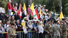 حشود من اللبنانيين من رجال ونساء يقفون على جانب الطريق وخلف حواجز وهم يحملون أعلام الفاتيكان والأعلام اللبنانية للترحيب ببابا الفاتيكان الزائر الباب ليو الرابع عشر.