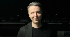 Siyah karanlık bir günde bir erkke siyah takım elbiseyle kameraya bakarak poz veriyor.