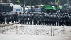 防暴警員手持盾牌，在仰光大學附近的街道上利用鐵線網布防