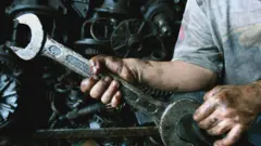 Sanayide çalışan bir çocuğun motor yağından kararmış elleri, kıyafetleri ve bazı motor parçaları görülüyor. 