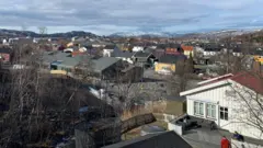 La ciudad de Kirkenes: varios edificios de una planta, calles y árboles, con colinas nevadas al fondo.