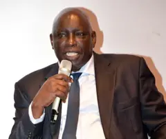Le journaliste et patron de presse sénégalais Madiambal Diagne, costume sombre, chemise blanche et cravatte bleue. Il tient un micro. 