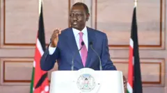 President Ruto speaking wit pink tie in front of a podium and two flags by di side