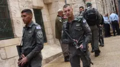 Israeli security officials stand behind tape at crime scene