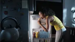 Une femme ouvre le frigo pour manger