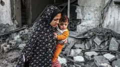 A woman holding a child flees following an Israeli strike in Rafah in the southern Gaza Strip on 23 November, 2023,