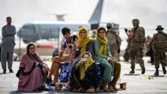 Afghans wave as they wait to board evacuation flights in Kabul