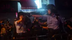 Cảnh sát chĩa súng vào những người biểu tình đang dùng gậy gộc đuổi theo họ